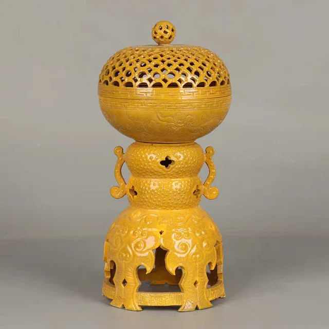 A yellow decorative vessel has a pierced domed lid and an openwork pedestal form