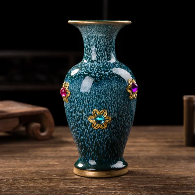 The pictured dark green vase has a flared mouth and small colorful floral ornaments edged in gold tones